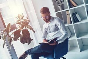 Young and smart. Handsome young man is smart casual wear writing something down while working in the office photo