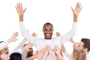 They chose their leader. Happy young African man standing against white background and keeping arms outstretched while group of excited people stretching hands to him and smiling photo