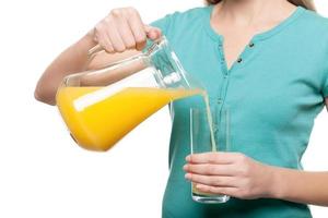 Pouring fresh juice. Cropped image of woman pouring juice into glass while standing isolated on white photo