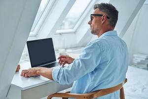 Confident mature man working on laptop while sitting at the office desk photo