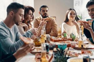 deliciosa pizza grupo de jóvenes con ropa informal comiendo pizza mientras cenan en el interior foto