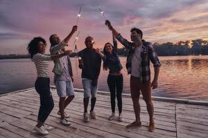 Creating happy memories. Full length of young people in casual wear smiling and holding sparkers while standing on the pier photo