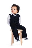 I will just sit here and do nothing Little African baby boy looking away while sitting on stool against white background photo