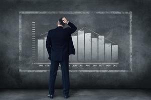 Hard decisions every day. Rear view of mature businessman scratching his head while standing against grey background with illustration of chart photo