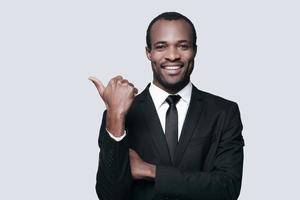 Successful choice. Handsome young African man in formalwear pointing away and smiling while standing against grey background photo
