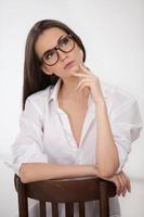 Thoughtful beauty. Attractive young woman holding her hand on chin and looking away while sitting on the chair photo