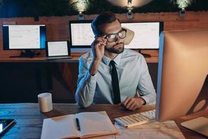 Confident young man working on computer while staying late in the office photo