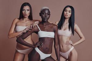 Proud to be beautiful. Three attractive mixed race women looking at camera while standing against brown background photo