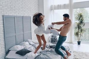 Just for fun. Happy young couple having a fun pillow fight while spending carefree time in the bedroom photo