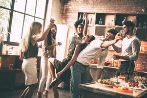 disfrutando de la mejor fiesta. jóvenes alegres bailando y bebiendo mientras disfrutan de una fiesta en casa en la cocina foto