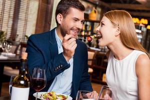 Try this Beautiful young loving couple enjoying dinner at the restaurant while man feeding his girlfriend with salad photo