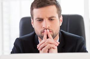 Concentrated at work. Handsome young man formalwear looking at laptop while sitting at his working place photo