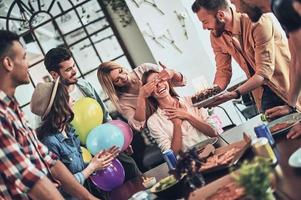 Top view of young people in casual wear gesturing and smiling while having a dinner party indoors photo