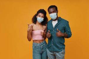 Beautiful young African couple in protective face masks looking at camera photo