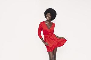 Beautiful young African woman in red dress dancing against background photo