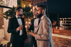 Three handsome men in suits drinking whiskey and communicating while spending time on party photo