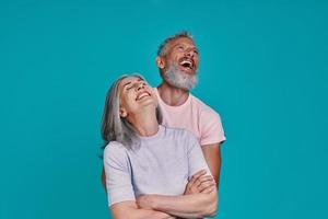 Happy senior couple bonding and laughing while standing together against blue background photo