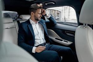 So tired. Frustrated young man in formalwear keeping eyes closed while sitting in the car photo