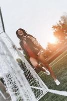 lista para jugar toda la longitud de una atractiva joven en bikini rojo posando cerca del poste de gol en el campo de fútbol foto