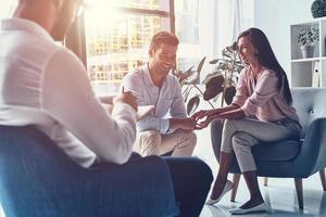 Happy to solve the problem. Young married couple talking and smiling while sitting on the therapy session with psychologist photo