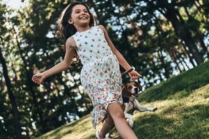 New adventures are coming. Cute little girl running and smiling while playing with her dog outdoors photo