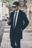 You have new message Handsome young well-dressed man in sunglasses using his smart phone while walking outdoors photo