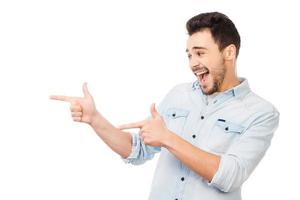 Cheerful presenter on your advertisement. Handsome young man in shirt pointing away while standing against white background photo