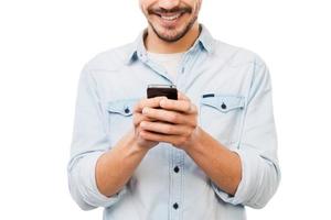 Communicative person. Cropped picture of handsome young man holding mobile phone and smiling while standing against white background photo