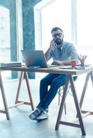 Discussing some business issues. Confident young beard man talking on the mobile phone while sitting at his working place in office photo