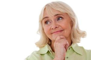 Lost in thoughts. Thoughtful senior woman holding hand on chin and looking away while standing isolated on white background photo