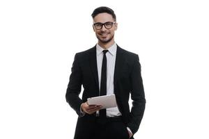 Always ready to help. Good looking young man in full suit holding digital tablet and smiling while standing against white background photo