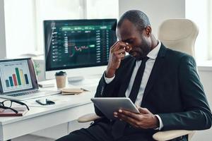 Tired young African man in formalwear using modern technologies while working in the office photo