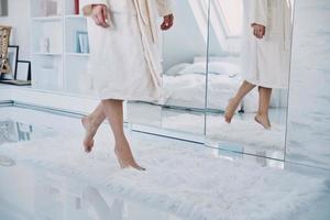 Close-up of barefoot woman wearing bathrobe walking in front of the large mirror at home photo