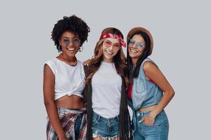 tres mujeres jóvenes atractivas sonriendo y mirando a la cámara mientras están de pie contra el fondo gris foto