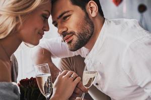 Love is in the air. Beautiful young couple drinking champagne and smiling while sitting face to face in the bedroom