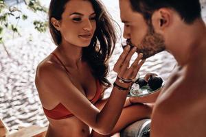 bella joven alimentando a sus novios con un trozo de higo dulce mientras descansan juntos en la playa foto