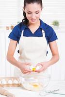 Making homemade pastry. Attractive young woman cracking egg into a bowl photo