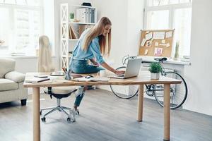 Beautiful young woman in smart casual wear using laptop while working in the office photo