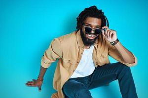 Top view of smiling young African man in casual wear adjusting eyewear and looking at camera while sitting against blue background photo