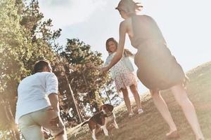 verano lleno de alegría. feliz familia joven de tres jugando con perro mientras pasa tiempo al aire libre foto