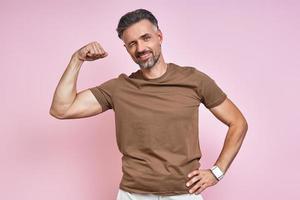 Handsome mature man showing his bicep and winking while standing against pink background photo