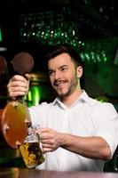 Got some beer Cheerful young bartender pouring beer and looking away photo
