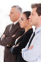 Successful business team. Side view of confident people in formalwear keeping arms crossed while standing in a row and looking away photo