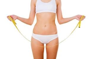 Woman with measuring tape. Cropped image of woman in underwear holding measuring tape while standing isolated on white photo