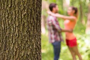 Loving couple in park. Close-up image of tree trunk and loving couple hugging in the background photo
