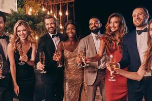 grupo de personas en ropa formal brindando con champán y sonriendo mientras pasan tiempo en una fiesta de lujo foto