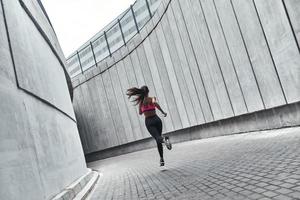 empujando fuerte vista trasera completa de una mujer joven con ropa deportiva trotando mientras hace ejercicio al aire libre foto