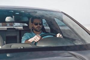 Driving carefully. Handsome young man looking straight while driving a status car photo