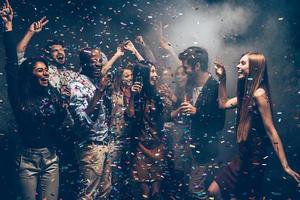 Fun and fun again. Group of beautiful young people throwing colorful confetti and looking happy photo