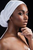 African beauty. Beautiful African woman wearing a headscarf and holding hand on chin while standing against black background photo